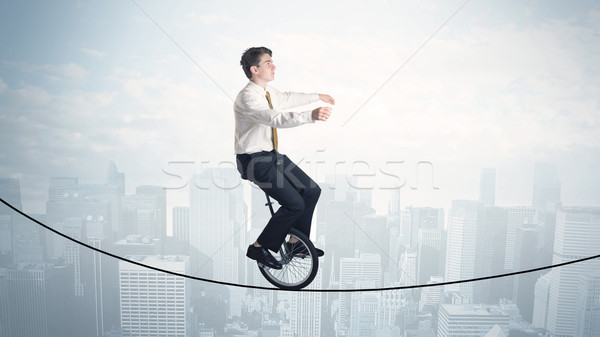 Stock photo: Brave guy riding a monocycle on a rope above cityscape