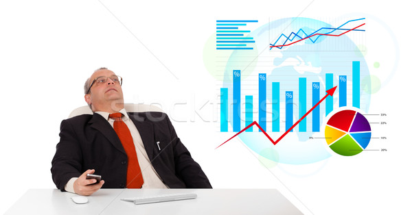 Businessman sitting at desk with statistics and holding a mobilephone, isolated on white Stock photo © ra2studio