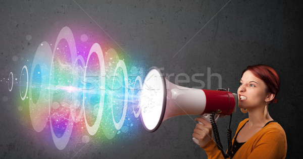 Cute young girl yells into a loudspeaker and colorful energy beam comes out Stock photo © ra2studio