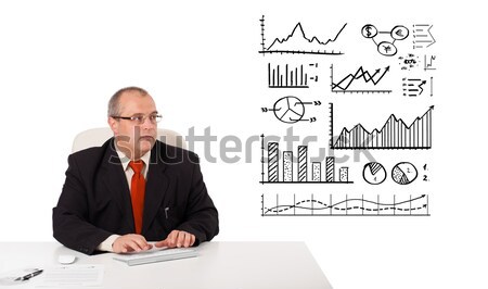 Businessman sitting at desk with diagrams and holding a mobilephone, isolated on white Stock photo © ra2studio