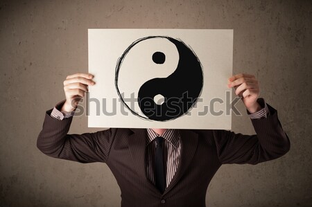 Businessman holding a paper with a yin-yang on it in front of hi Stock photo © ra2studio