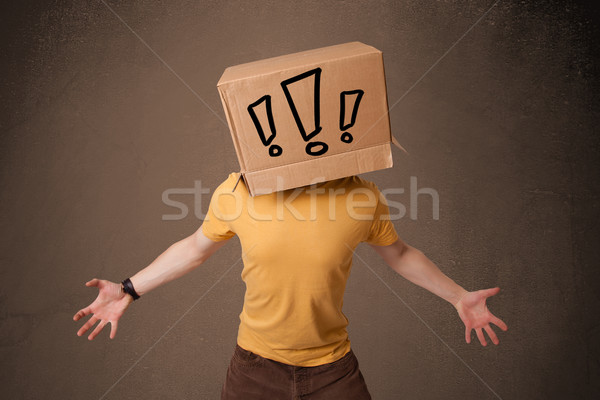 Young man gesturing with a cardboard box on his head with exclam Stock photo © ra2studio
