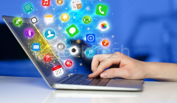 Stock photo: Hand pressing modern laptop with mobile app icons and symbols