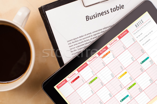 Workplace with tablet pc showing calendar and a cup of coffee on a wooden work table closeup Stock photo © ra2studio