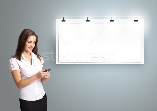 Beautiful young woman standing next to a modern copy space and holding a phone Stock photo © ra2studio