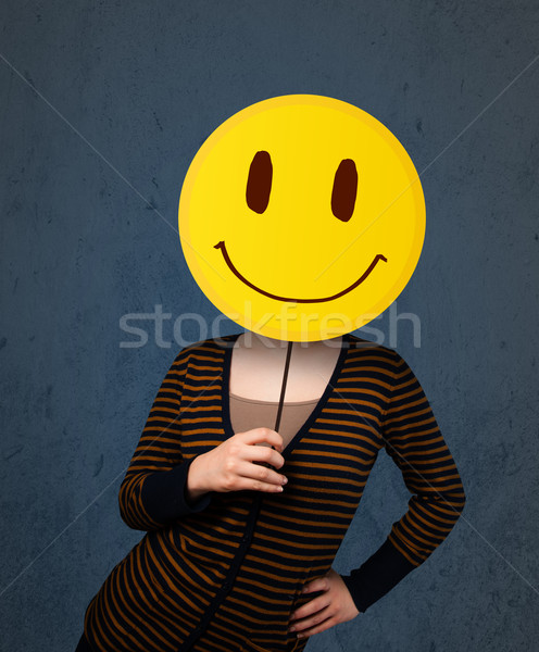 Stock photo: Young woman holding a smiley face emoticon