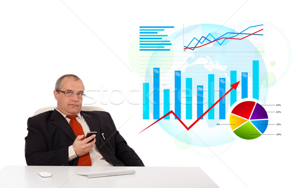Businessman sitting at desk with statistics and holding a mobilephone, isolated on white Stock photo © ra2studio