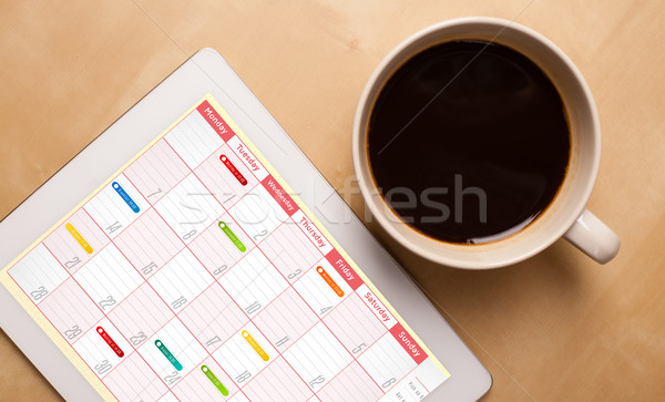 Workplace with tablet pc showing calendar and a cup of coffee on a wooden work table closeup Stock photo © ra2studio