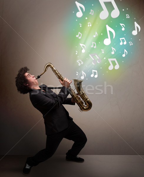 Young musician playing on saxophone while musical notes explodin Stock photo © ra2studio