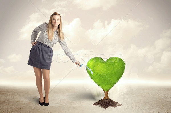 Business woman watering heart shaped green tree Stock photo © ra2studio