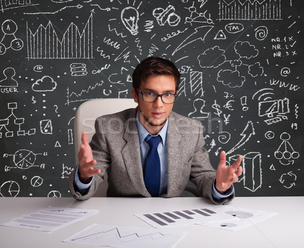 Businessman sitting at desk with business scheme and icons Stock photo © ra2studio