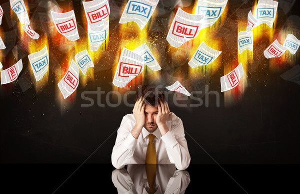 Stock photo: Depressed businessman sitting under burning tax and bill papers