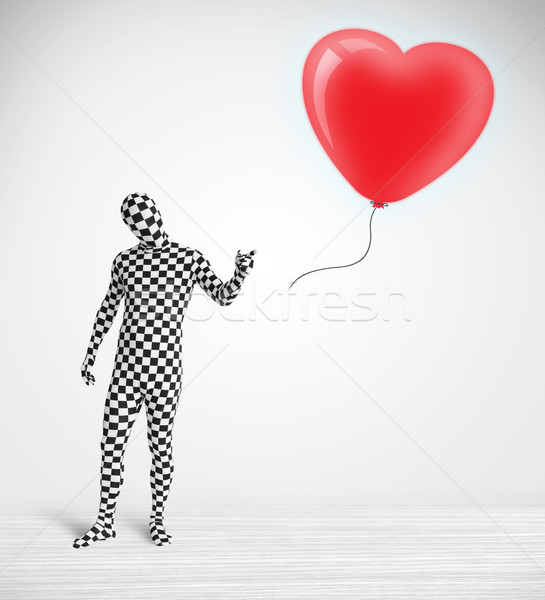 Cute guy in morpsuit body suit looking at a red balloon shaped heart Stock photo © ra2studio