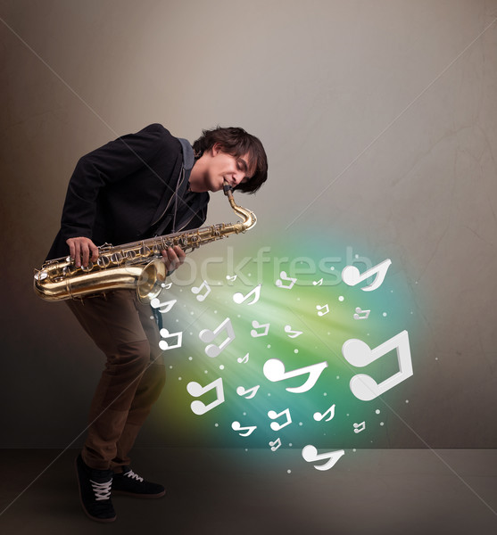 Young musician playing on saxophone while musical notes explodin Stock photo © ra2studio