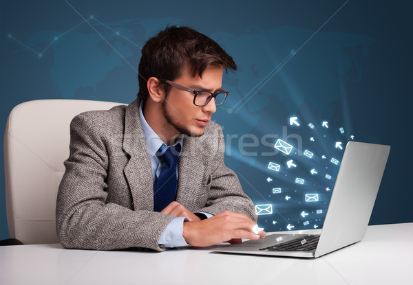Attractive young man sitting at dest and typing on laptop with message icons comming out Stock photo © ra2studio