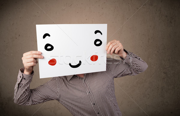 Stock photo: Businessman holding a cardboard with a smiley face on it