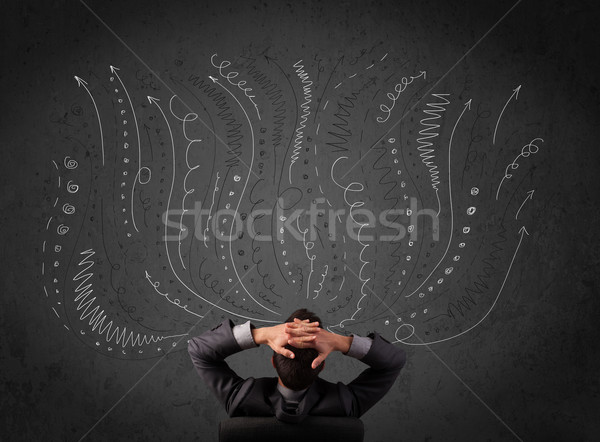 Thoughtful young businessman sitting and deciding in front of a chalkboard with sketched arrows Stock photo © ra2studio