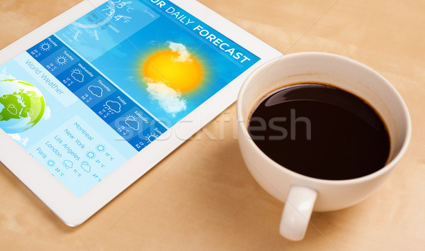 Workplace with tablet pc showing weather forecast and a cup of coffee on a wooden work table closeup Stock photo © ra2studio
