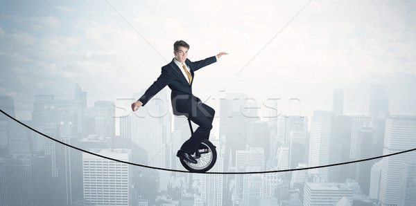 Brave guy riding a monocycle on a rope above cityscape Stock photo © ra2studio