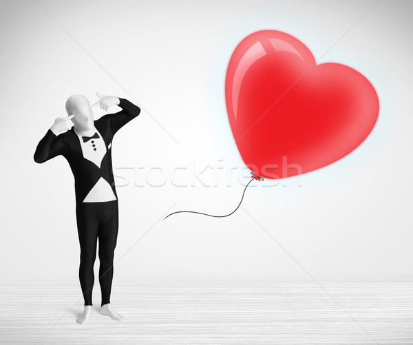 Cute guy in morpsuit body suit looking at a red balloon shaped heart Stock photo © ra2studio