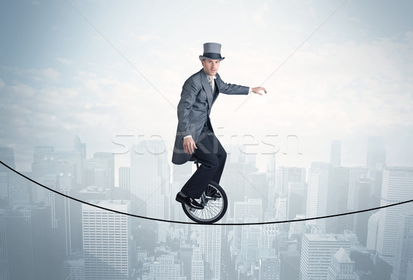 Brave guy riding a monocycle on a rope above cityscape Stock photo © ra2studio