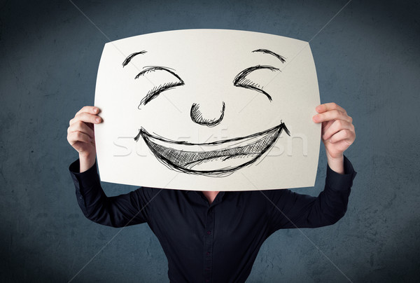 Businessman holding a paper with smiley face in front of his hea Stock photo © ra2studio