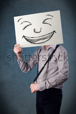Businessman holding a paper with smiley face in front of his hea Stock photo © ra2studio
