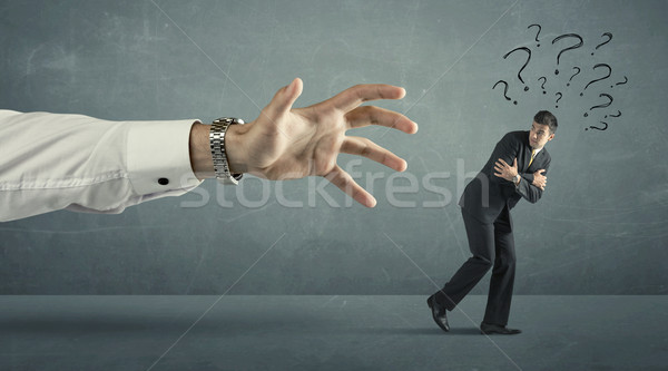 Stock photo: Businessman with question marks running away from a big hand 