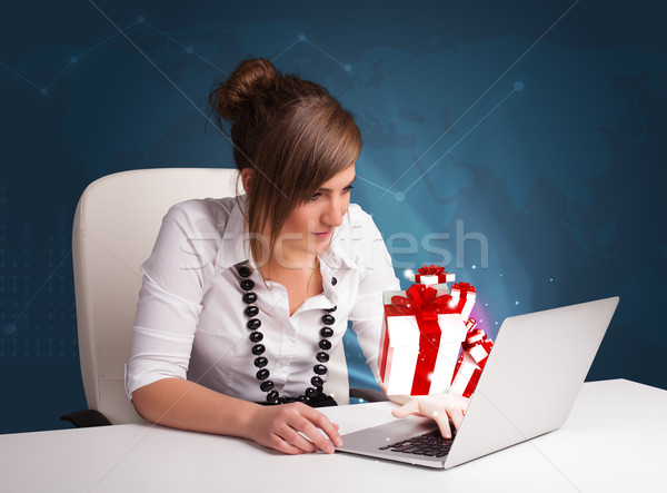 Pretty young lady sitting at desk and typing on laptop with present boxes icons Stock photo © ra2studio