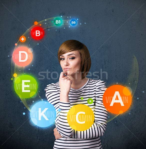 Stock photo: Young woman thinking with vitamins circulation around her head