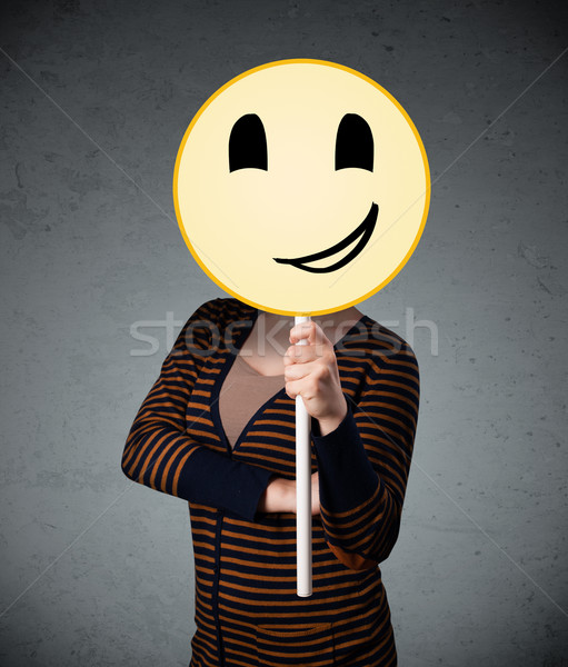 Stock photo: Young woman holding a smiley face emoticon