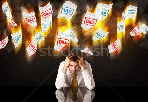 Stock photo: Depressed businessman sitting under burning tax and bill papers