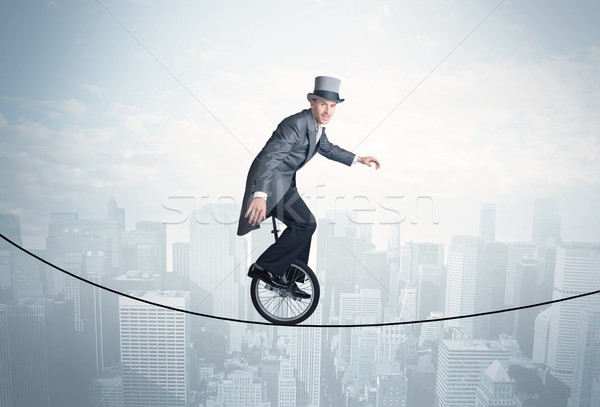 Brave guy riding a monocycle on a rope above cityscape Stock photo © ra2studio