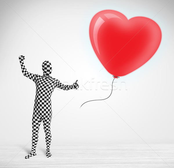 Cute guy in morpsuit body suit looking at a red balloon shaped heart Stock photo © ra2studio