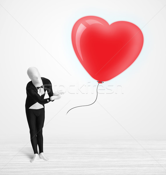 Cute guy in morpsuit body suit looking at a red balloon shaped heart Stock photo © ra2studio