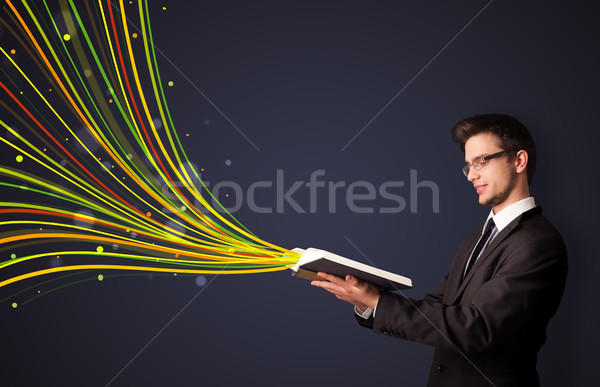 Young man reading a book while colorful lines are coming out of the book Stock photo © ra2studio