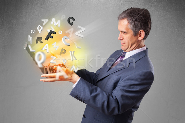 Middle aged businessman holding laptop with colorful letters Stock photo © ra2studio
