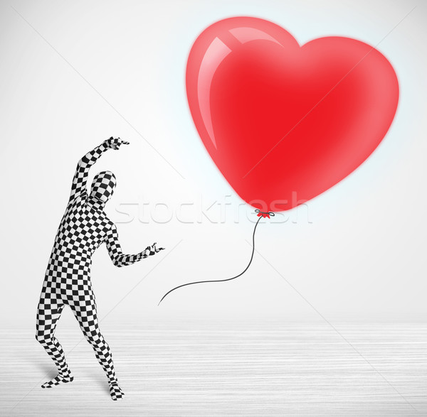 Cute guy in morpsuit body suit looking at a red balloon shaped heart Stock photo © ra2studio