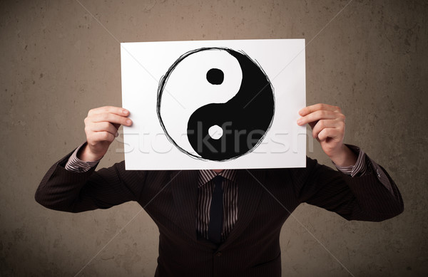 Businessman holding a paper with a yin-yang on it in front of hi Stock photo © ra2studio