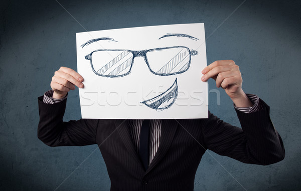 Businessman holding a paper with smiley face in front of his hea Stock photo © ra2studio