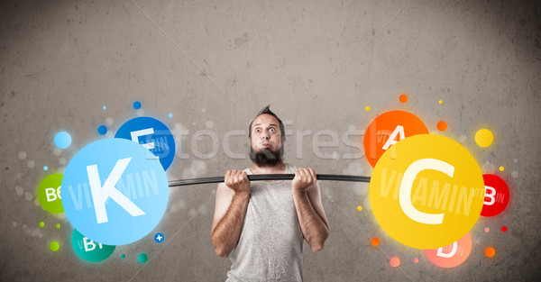 Stock photo: skinny guy lifting colorful vitamin weights