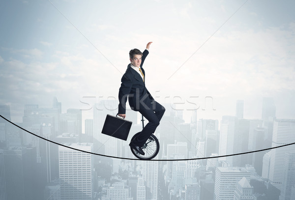 Brave guy riding a monocycle on a rope above cityscape Stock photo © ra2studio