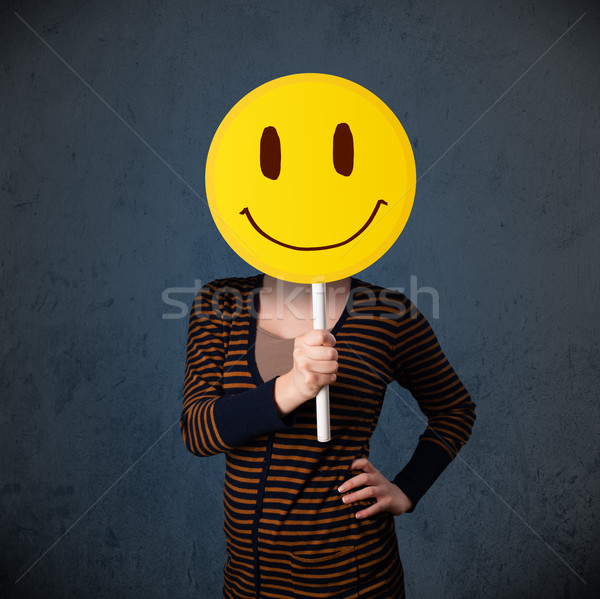 Young woman holding a smiley face emoticon Stock photo © ra2studio