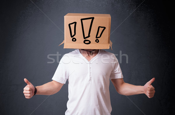 Stock photo: Young man gesturing with a cardboard box on his head with exclam