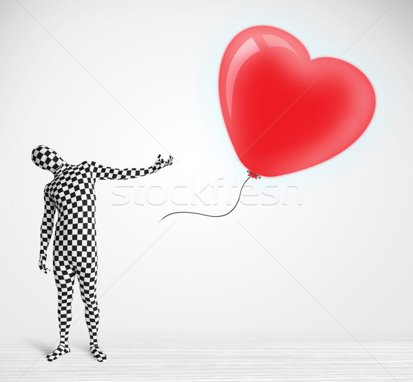 Cute guy in morpsuit body suit looking at a red balloon shaped heart Stock photo © ra2studio