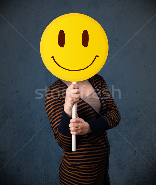 Young woman holding a smiley face emoticon Stock photo © ra2studio