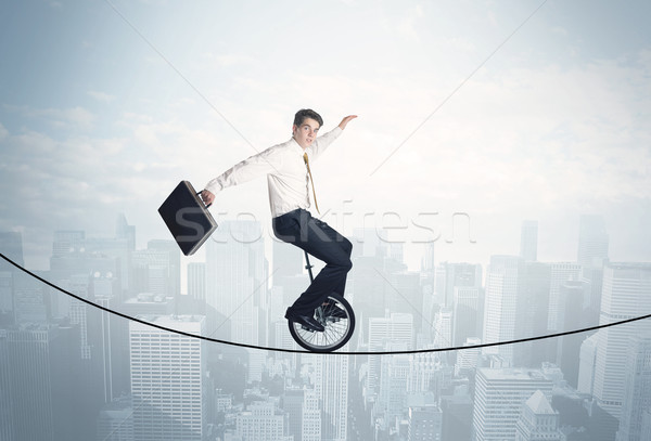 Brave guy riding a monocycle on a rope above cityscape Stock photo © ra2studio