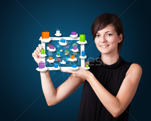 Stock photo: beautiful woman holding modern tablet with colorful shopping bags on clouds