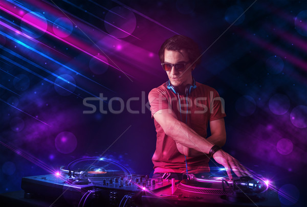 Young DJ playing on turntables with color light effects Stock photo © ra2studio