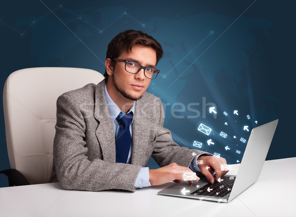 Attractive young man sitting at dest and typing on laptop with message icons comming out Stock photo © ra2studio